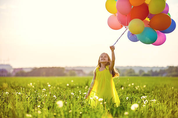 Girl in a yellow dress holding colorful balloons in a summer field